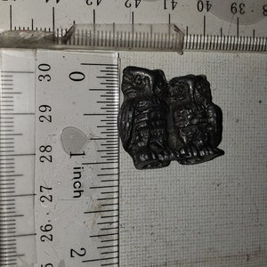 May include: A black metal owl figurine, approximately 1 inch in size, with detailed carvings. The owl is perched on a white surface with a ruler for scale.