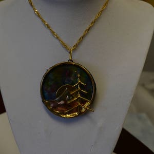 May include: A gold chain necklace with a round pendant featuring a multi-colored landscape scene with a tree silhouette.
