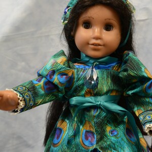 May include: A doll wearing a teal and green peacock-patterned dress with a teal sash and a crown with blue jewels. The doll has long black hair and brown eyes.