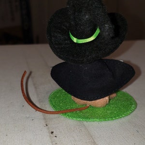 K&ouml;nnte beinhalten: Handgemachte Halloween-Dekoration mit einer kleinen Hexenfigur. Die Hexe hat einen schwarzen Hut mit gr&uuml;nem Band, ein schwarzes Kleid und einen braunen Schwanz. Sie sitzt auf einem gr&uuml;nen Filzkreis.
