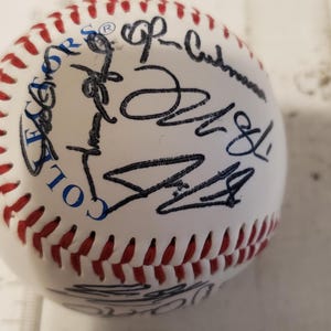 May include: White baseball with red stitching and blue text that reads "Collector's Edition". The ball is signed in black ink by multiple people.