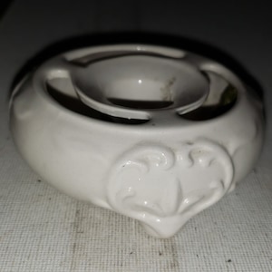 May include: White ceramic incense burner with a decorative design. The burner has a central opening for incense sticks and a raised rim around the top.