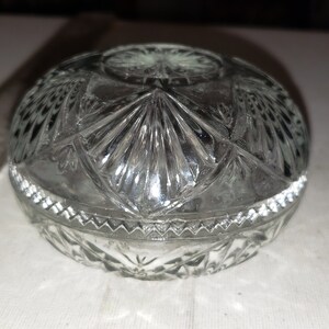 May include: A clear glass lidded trinket box with a cut glass design. The lid has a raised center with a starburst pattern.