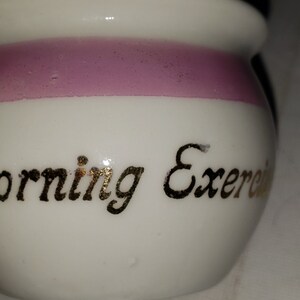 May include: White ceramic jar with a pink band around the middle. The jar has gold lettering that reads "Morning Exercise".
