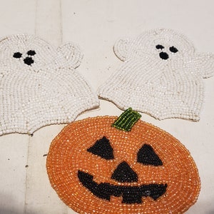 May include: Three Halloween-themed beaded ornaments: two white ghosts and one orange pumpkin with a black jack-o'-lantern face.