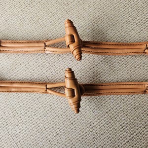 Puede incluir: Dos pares de gemelos de cuero marrón claro. Cada gemelo presenta un extremo anudado, un elemento decorativo central y una barra de conexión. El cuero está cosido con hilo oscuro, y el diseño es simétrico.