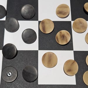 Peut inclure: Un jeu de dames avec des cases noires et blanches. Des pions gris foncé sont sur les cases noires et des pions brun clair sur les cases blanches. Les pions sont ronds et plats.