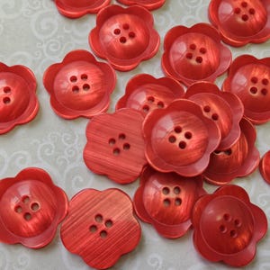 Peut inclure: Plusieurs boutons rouges en forme de fleur, chacun avec quatre trous. Les boutons ont une finition nacrée et sont dispersés sur une surface à motifs. Ces boutons décoratifs sont parfaits pour la couture et les travaux manuels.