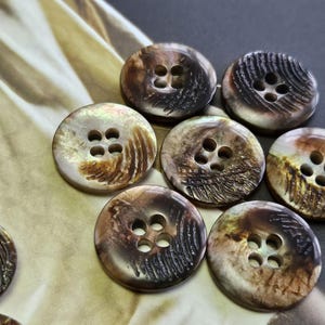May include: A selection of round, iridescent buttons, each with four holes. The buttons display a natural, organic aesthetic with brown, tan, and cream hues. Some buttons have etched patterns. Suitable for sewing and craft activities.