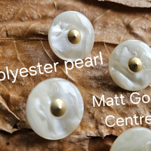 May include: Four round polyester pearl buttons with a matte gold centre. The buttons have a pearlescent white finish. The image includes the text "Polyester pearl" and "Matt Gold Centre".