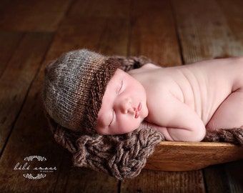 May include: A newborn baby sleeping in a brown woven basket, wearing a brown and gray knitted hat. The baby is curled up in a fetal position with their arms tucked in.