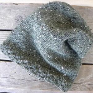 May include: A green knitted beanie with a flecked texture. The beanie has a folded brim and a loose, slouchy fit.