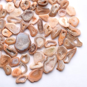 May include: A collection of polished agate geodes in various shapes and sizes. The geodes display a range of colors, including beige, cream, and light brown, with crystalline interiors. Some geodes have a hollow center, while others are solid.