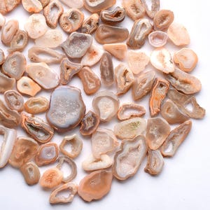 Op de afbeelding: Een verzameling gepolijste agaatgeodes in verschillende vormen en maten. De geodes tonen een reeks kleuren, waaronder beige, crème en lichtbruin, met kristallijne interieurs. De opstelling is cirkelvormig en toont de natuurlijke schoonheid van de stenen.