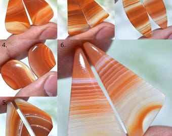 May include: A collection of polished agate stones in various shapes, including teardrop, oval, and triangular. The stones display bands of orange and white, with a translucent quality. The stones are held in a person's hand.