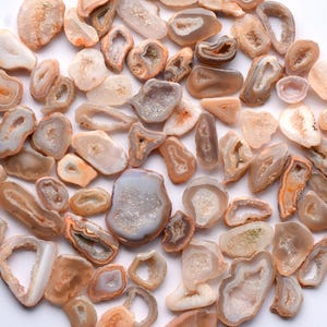May include: A selection of polished agate geodes in diverse shapes and sizes. The geodes exhibit a spectrum of colours, including beige, brown, and white, with crystalline interiors. Some geodes have open cavities, revealing the inner crystal formations.