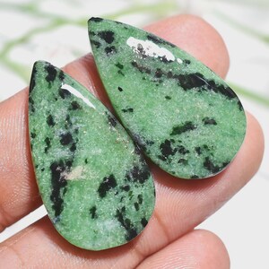 May include: Two polished, pear-shaped cabochons featuring a vibrant light green base color with distinct, irregular black mineral inclusions scattered throughout the surface, showcasing a smooth, reflective finish on both gemstone pieces.