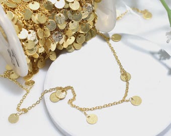 May include: A spool of gold-colored chain with attached round, flat sequins. A length of the chain is laid out, showing the delicate links and the dangling sequins. The chain is on a white surface.