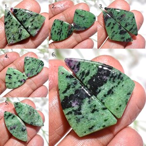 May include: A selection of polished gemstone pairs in different shapes. The stones have a green base with black and red inclusions. The gemstones are shown against a neutral backdrop, highlighting their natural patterns and textures.