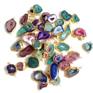 Puede incluir: Una colección de colgantes de piedras preciosas de ágata de colores con bordes dorados. Los colgantes presentan una variedad de colores, incluyendo turquesa, morado, rosa y azul. Cada piedra tiene un patrón y forma únicos, ideal para la creación de joyas.
