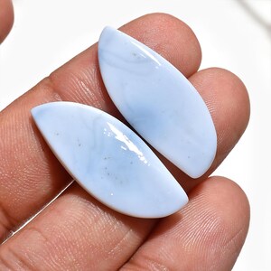 May include: Two polished, marquise-shaped blue chalcedony gemstones with a smooth, glossy surface. The stones exhibit a soft, pale blue colour with subtle, milky white swirling patterns throughout their translucent, cabochon-cut bodies.