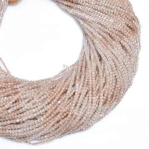 May include: Close-up of strands of small, round, light brown beads. The beads are strung together, creating a cascading effect. The beads are uniform in size and shape, with a slightly faceted surface. The text "By STONAA" is visible.