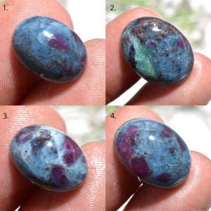 May include: Four oval-shaped gemstones with a mix of blue-gray and deep red hues. The stones have a polished, smooth surface, with the red appearing in patches and inclusions within the blue-gray matrix. The gemstones are likely used for jewelry.
