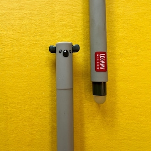 May include: Two gray pens on a yellow background. One pen features a koala bear design on the top. The other pen has the word "LEGAMI MILANO" printed on it. The pens are designed for writing and/or use on a touch screen.
