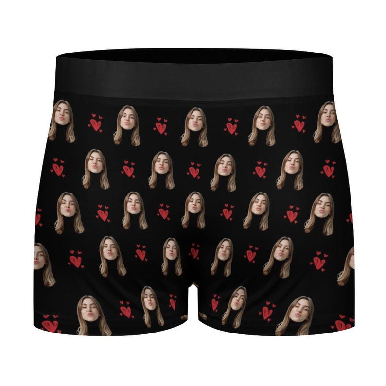 May include: Black boxer briefs with a repeating pattern of a woman's face and red hearts. The boxer briefs have a black waistband and are made of a soft, comfortable material.