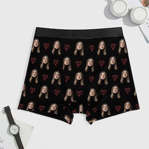 May include: Black boxer briefs with a repeating pattern of a woman's face and red hearts. The briefs have a black waistband and are made of a soft, comfortable material. A unique and personalized gift idea.