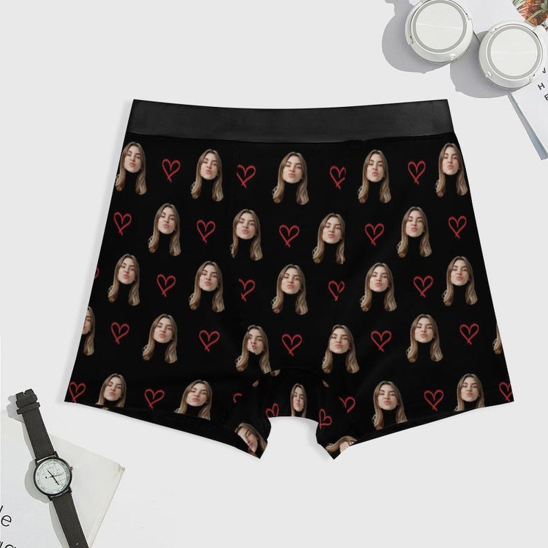 May include: Black boxer briefs with a repeating pattern of a woman's face and red hearts. The briefs have a black waistband and are made of a soft, comfortable material. A unique and personalized gift idea.