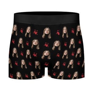 May include: Black boxer briefs with a repeating pattern of a woman's face and red hearts. The woman is wearing a black turtleneck and making a kissing face. The waistband is solid black.