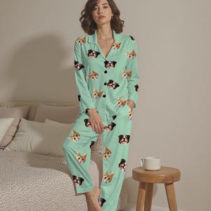 May include: A mint green pajama set featuring a repeating pattern of cat and dog faces. The long-sleeved top has a collared neckline and button-down front. The pants have a relaxed fit. The pajama set is made of a soft, comfortable material.