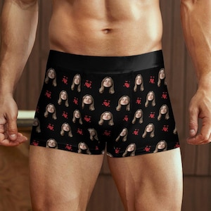 May include: Black boxer briefs with a repeating pattern of a woman's face and red hearts. The underwear has a black waistband and is made of a soft, comfortable material.