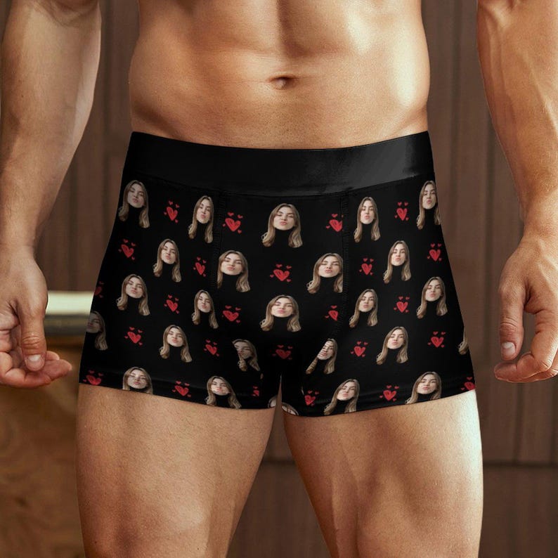 May include: Black boxer briefs with a repeating pattern of a woman's face and red hearts. The underwear has a black waistband and is made of a soft, comfortable material.