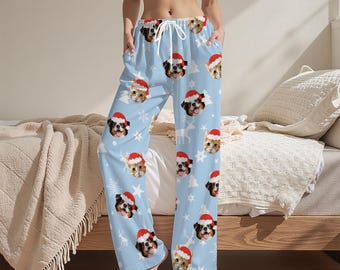 Könnte beinhalten: Hellblaue Schlafanzughose mit einem sich wiederholenden Muster aus Hunden und Katzen mit Weihnachtsmützen, Schneeflocken und Rentieren. Die Hose hat einen Kordelzug in der Taille und Taschen.