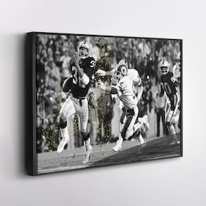 May include: Black and white framed print of a football game in action. A player in a black uniform with the number 31 runs with the ball, pursued by players in white and gold uniforms.