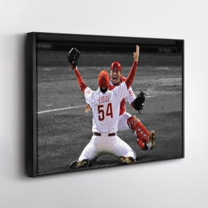 May include: A framed photograph captures a celebratory moment in baseball. Two players in red and white uniforms with the number 54 and the name "Lidge" are celebrating a victory. The background is in grayscale.
