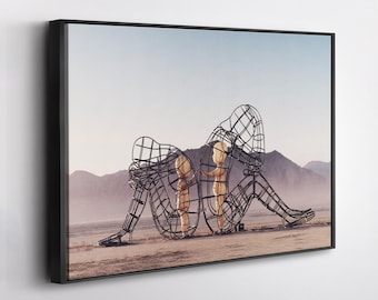 May include: Framed art print featuring two wireframe human figures in a desert landscape. The figures are seated, with one appearing to cradle their head. The background includes mountains and a pale blue sky.