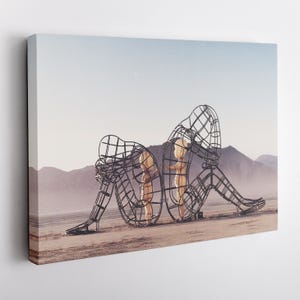 Puede incluir: Impresi&oacute;n en lienzo que presenta una obra de arte surrealista. Dos figuras de alambre sentadas encierran a dos figuras m&aacute;s peque&ntilde;as. El fondo muestra un paisaje des&eacute;rtico con monta&ntilde;as y un cielo azul p&aacute;lido.