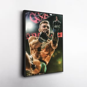 May include: A framed action shot of a mixed martial artist in a fighting stance, wearing black and blue UFC gloves. The athlete is shirtless, with tattoos visible, and is giving the middle finger. The background is blurred with red and yellow lights.