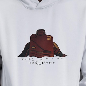 May include: White hoodie with a front pocket and a drawstring hood. The hoodie features a graphic of a football player in a red uniform with the number 2. The text "WHAT IS 2.2? HAIL MARY" is printed below the graphic.