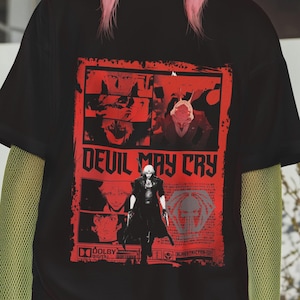 May include: A person wearing a black t-shirt with a red graphic that says "DEVIL MAY CRY". The person is also wearing a tan beanie and a green mesh long sleeve shirt.