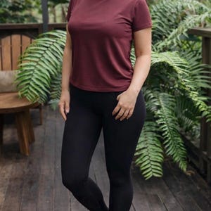 May include: A short-sleeved crew neck t-shirt in a solid dark maroon color paired with solid black leggings. The t-shirt features a standard fit with a rounded neckline and short sleeves, while the leggings are form-fitting and reach the ankles.