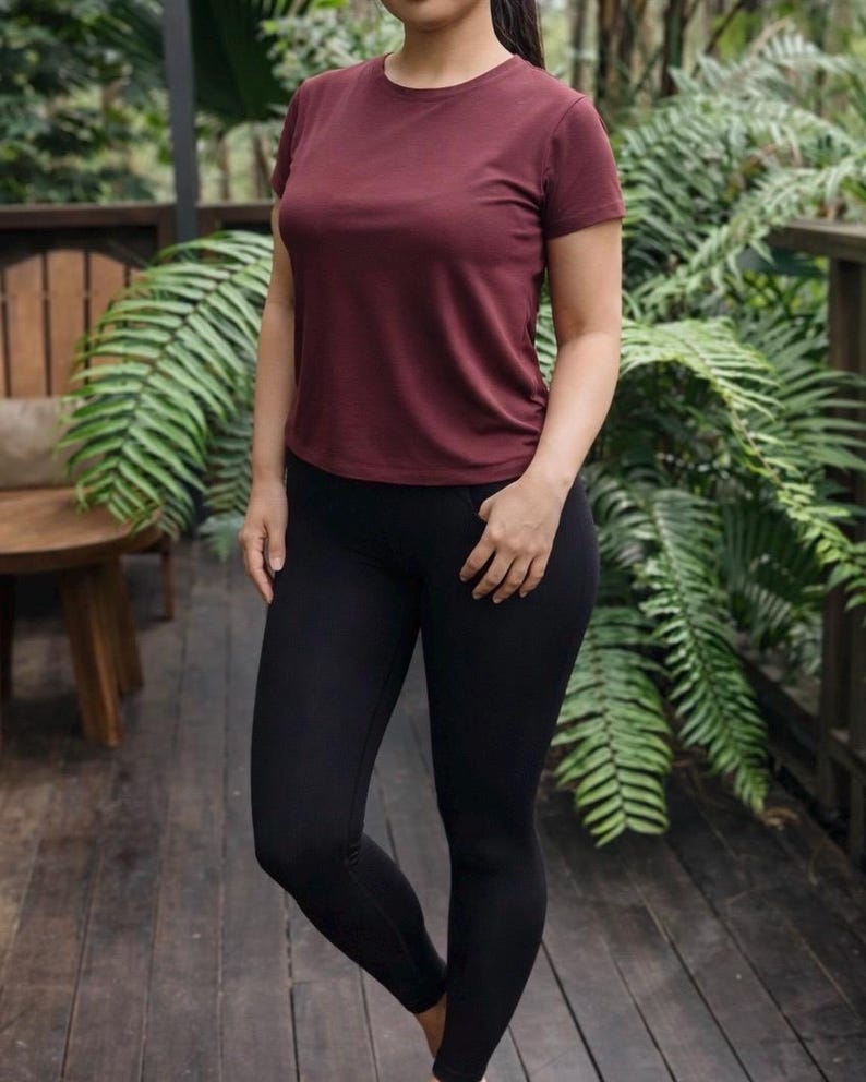 May include: A short-sleeved crew neck t-shirt in a solid dark maroon color paired with solid black leggings. The t-shirt features a standard fit with a rounded neckline and short sleeves, while the leggings are form-fitting and reach the ankles.