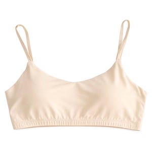May include: A beige bralette with thin spaghetti straps and a scoop neckline. The bottom hem features a ribbed band for a secure fit. The soft, neutral color makes it versatile for layering or wearing on its own.