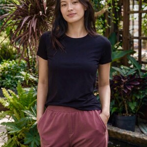 May include: A solid black short-sleeved crew neck t-shirt paired with solid dark mauve trousers featuring a high waistband and two side pockets. The t-shirt has a standard fit with a round neckline and short sleeves, while the trousers have a relaxed cut.