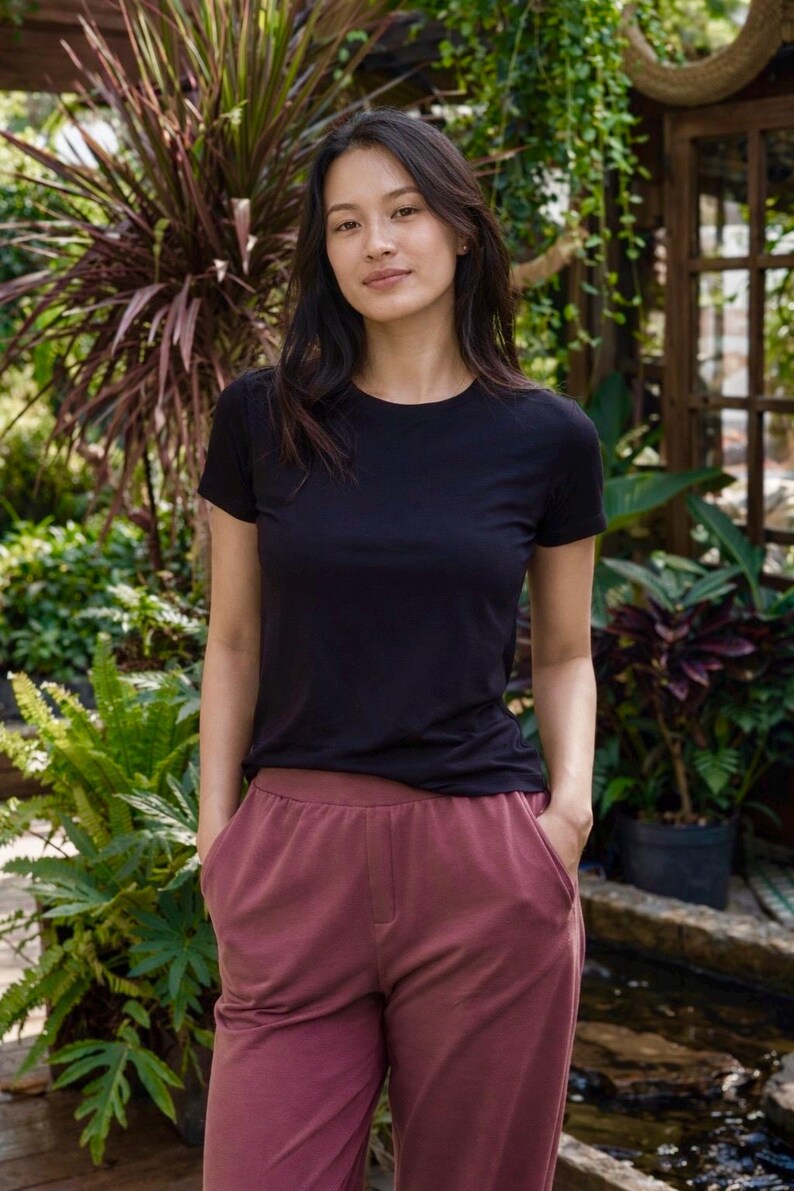 May include: A solid black short-sleeved crew neck t-shirt paired with solid dark mauve trousers featuring a high waistband and two side pockets. The t-shirt has a standard fit with a round neckline and short sleeves, while the trousers have a relaxed cut.