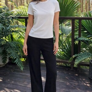 May include: A plain white short-sleeved t-shirt with a crew neckline paired with solid black wide-leg trousers. The t-shirt is fitted through the torso, while the trousers feature a relaxed, straight-cut silhouette that extends to the floor.