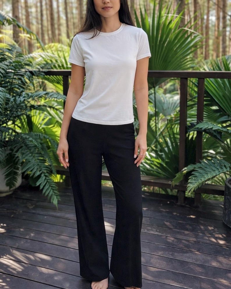 May include: A plain white short-sleeved t-shirt with a crew neckline paired with solid black wide-leg trousers. The t-shirt is fitted through the torso, while the trousers feature a relaxed, straight-cut silhouette that extends to the floor.